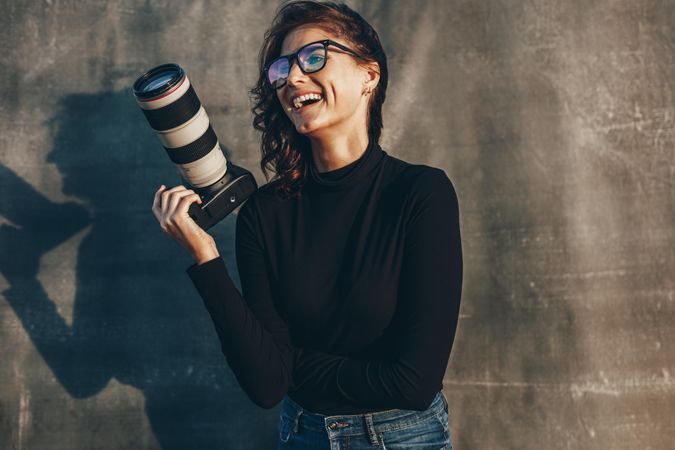 Woman photographer holding professional camera smiling against oliphant backdrop