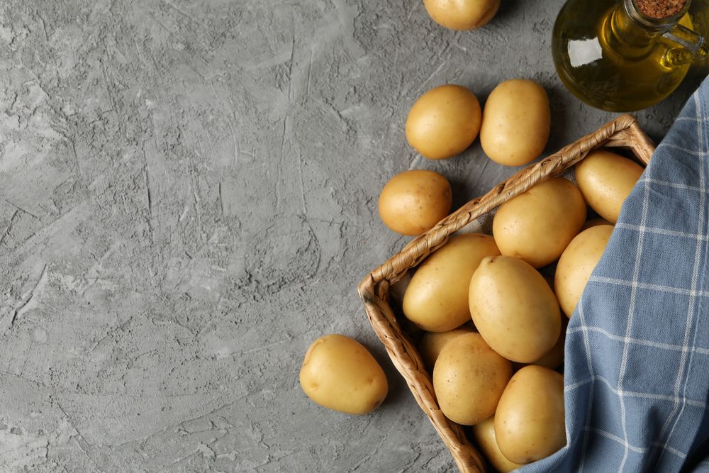 Looking down at wicker box of potatoes on marble table, copy space
