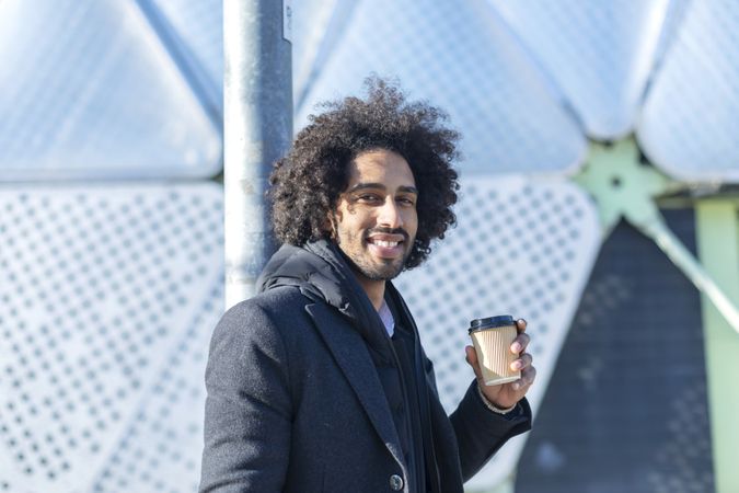 Portrait of smiling Black man in jacket with warm beverage standing outside