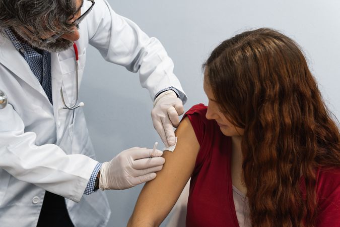 Mature doctor putting patch on arm of patient after injection