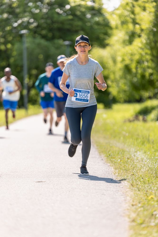 Female Leading Marathon Participants in a Race for the Finish Line: Group of People Running Through Park Health Trail and Participating in a Marathon with Dedication