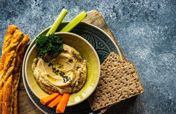 Top view of creamy hummus and chopped vegetables on grey kitchen counter with space for text