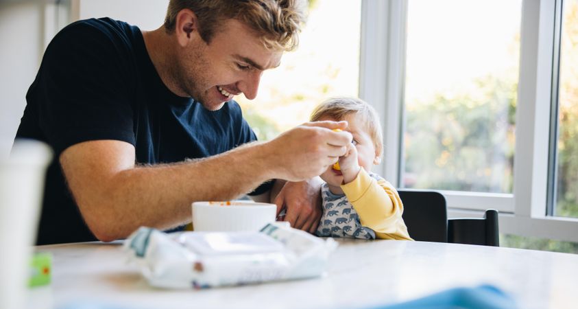 Loving father feeding his baby with a spoon while on paternity leave