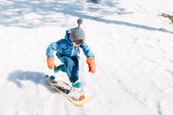 Kid jumping on board riding down snowy mountain