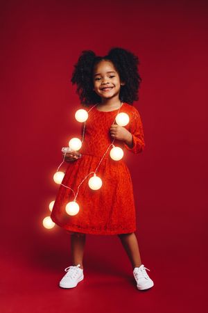 Beautiful girl in red dress holding string of lights around her neck