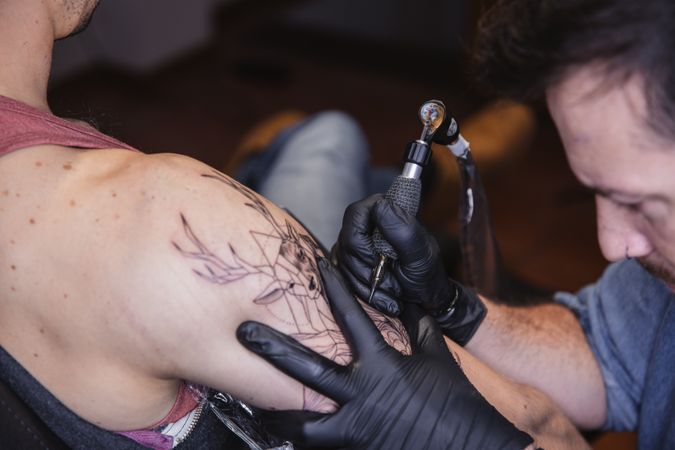 Master doing tattoo on forearm of male customer