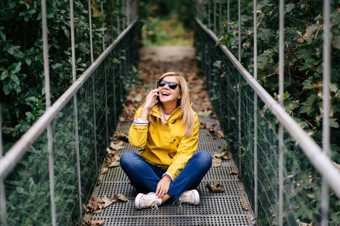 Happy female traveler talking phone on suspension bridge in summer