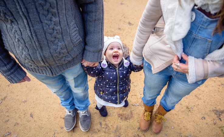 Cute girl looking up while holding her parents hand outside