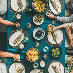 Flat-lay of human hands at table, beer glasses, grilled sea bass, square crop