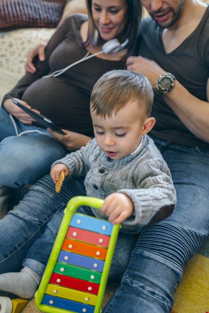 Pregnant woman and husband looking tablet while son plays