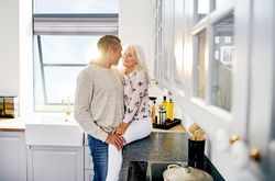 Grey haired woman sitting on kitchen counter with her husband