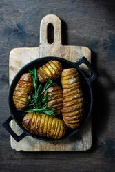 Top view of baked potato fans in iron cast pot on wooden board on kitchen counter