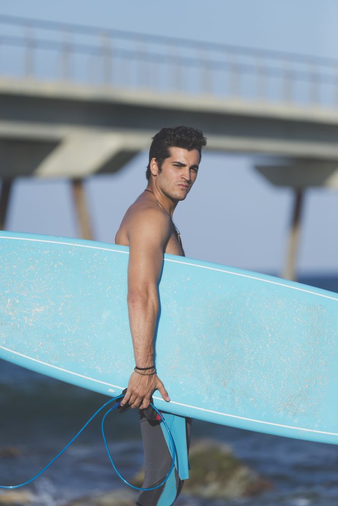 Male surfer with board standing on sunny coastline