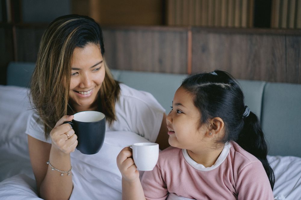 Mother and daughter having a morning hot drink in bedroom