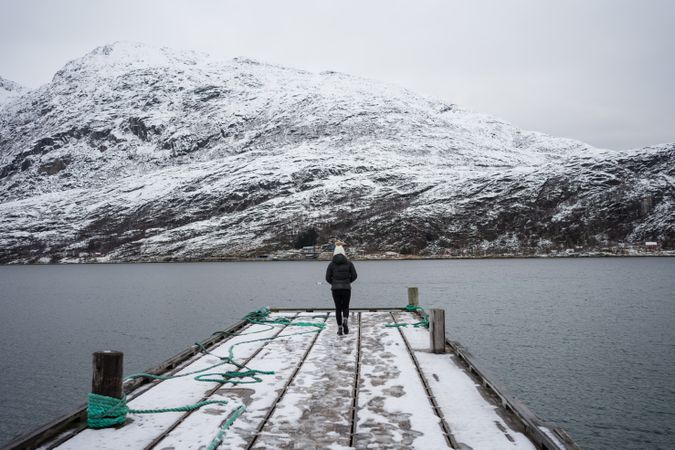 Woman on waterfront against small town at snowy foothill