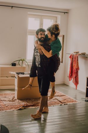 Happy couple piggybacking in room next to cardboard boxes