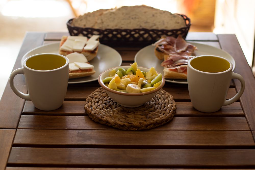 Breakfast in a house with bread, ham, cheese, fruit and coffee on a wood table.