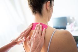 Physical therapist using kinesiology tape on upper back of patient