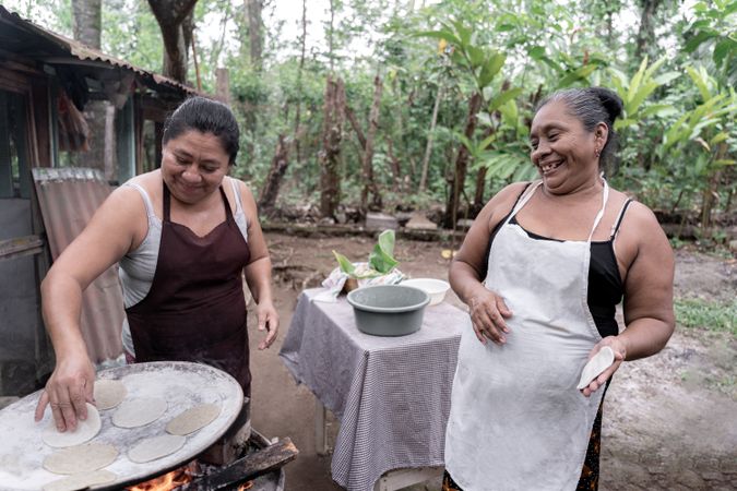 Two adult Hispanic women having fun while preparing corn tortillas