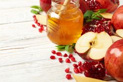 Glass honey pot with dipper, pomegranate seeds, and an apple in corner with copy space