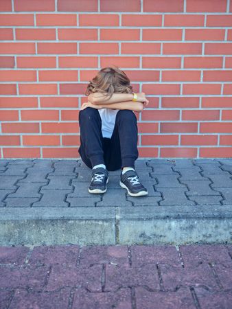 Unrecognizable boy hugging knees and sitting near brick wall