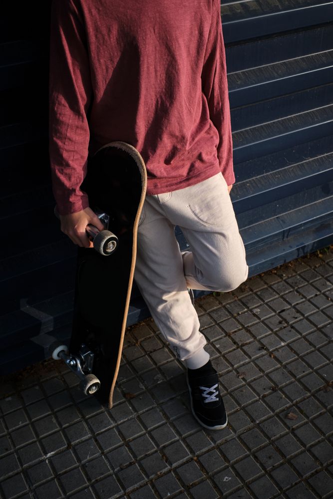 Crop skater leaning on wall on city street