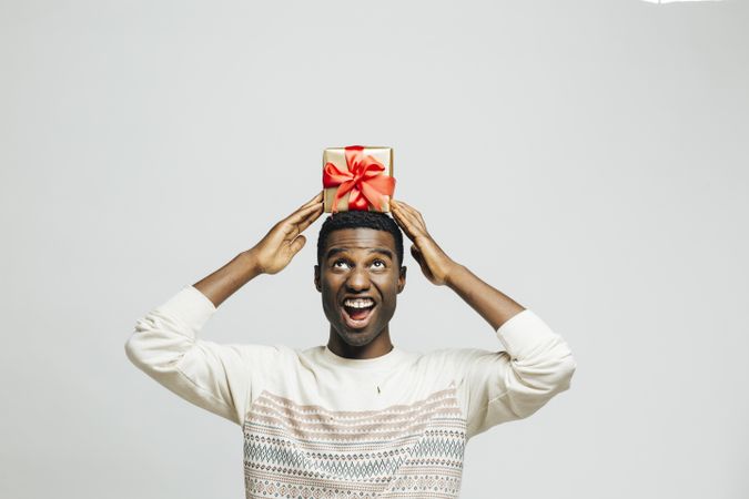Excited Black man holding gold box with red bow above his head
