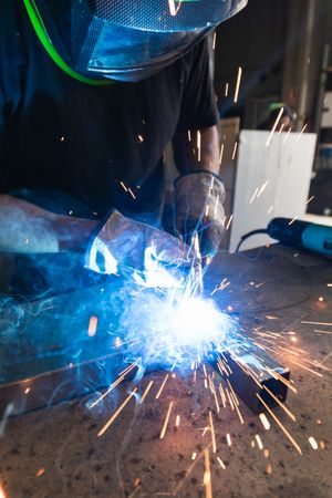 Welder in protective helmet welding metal detail in workshop