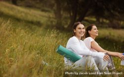 Two cheerful women friends sitting with yoga mats in the meadows 4BJVk4