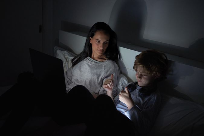 Mother and son watching film on laptop in dark room