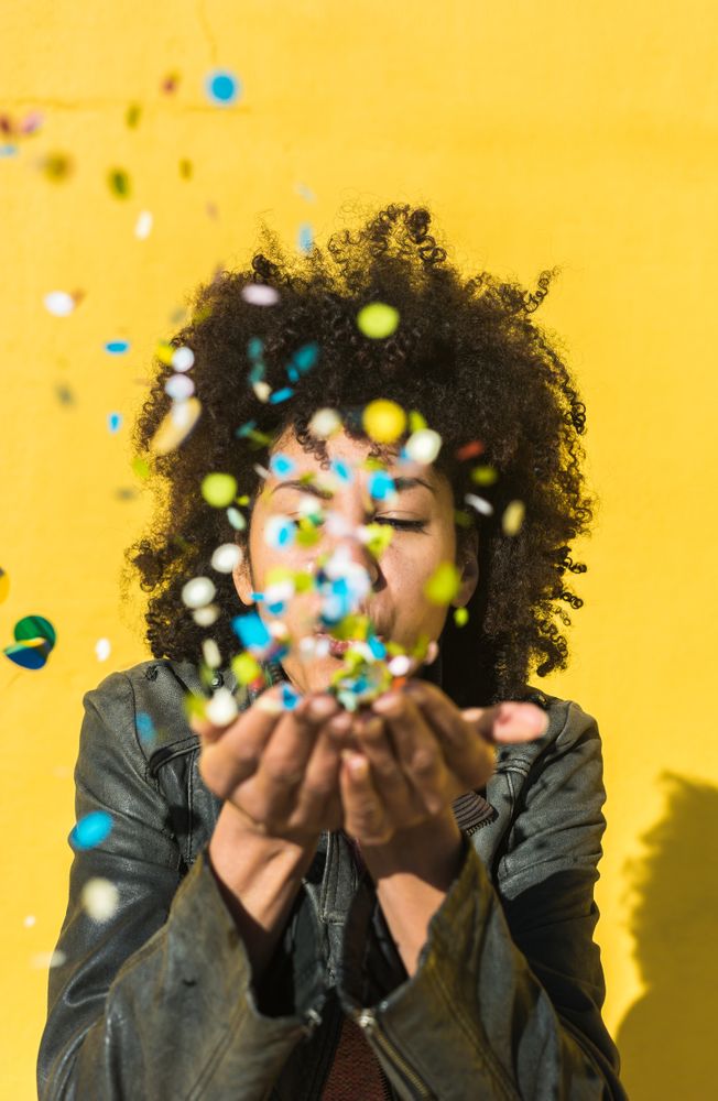 Black woman with afro hair celebrating with confetti.