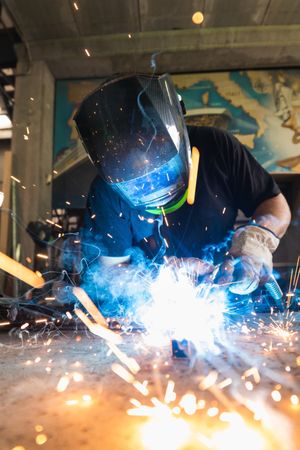 Welder in protective helmet welding metal detail in workshop