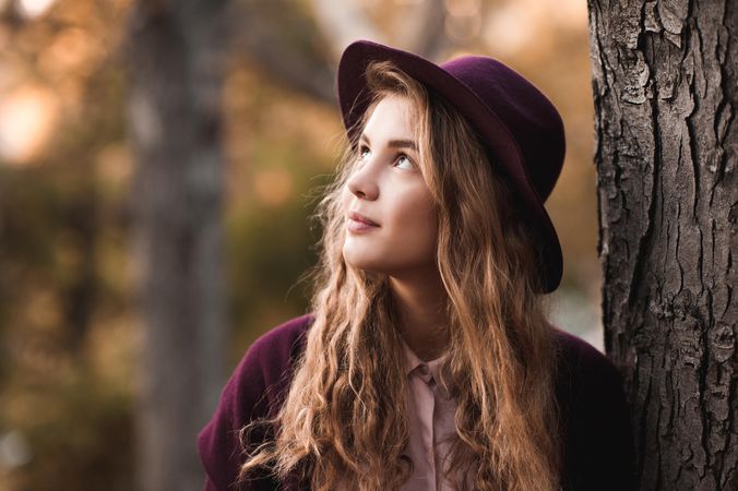 Portrait of teenage girl with purple hat beside tree looking up