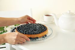 Woman hands hold tasty blueberry pie on table