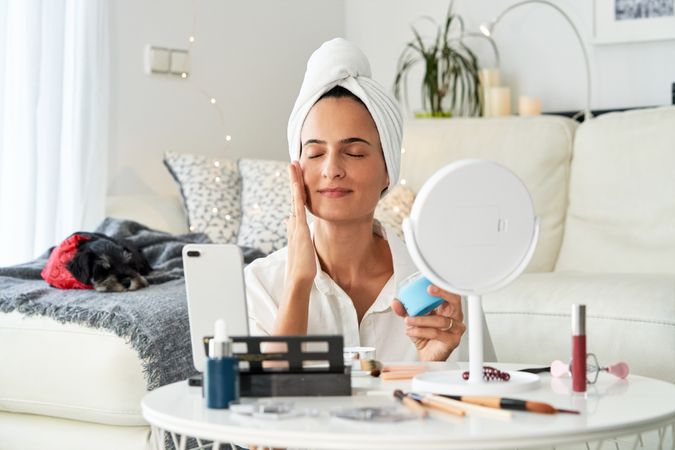 Female applying cream on face while recording video on smartphon