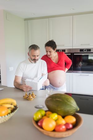 Pregnant woman and male partner deciding what to cook for dinner from recipe book