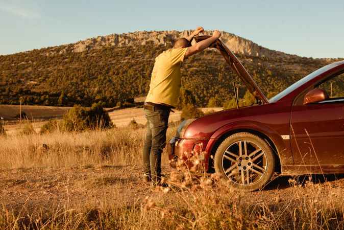 Anonymous man examining broken car in countryside
