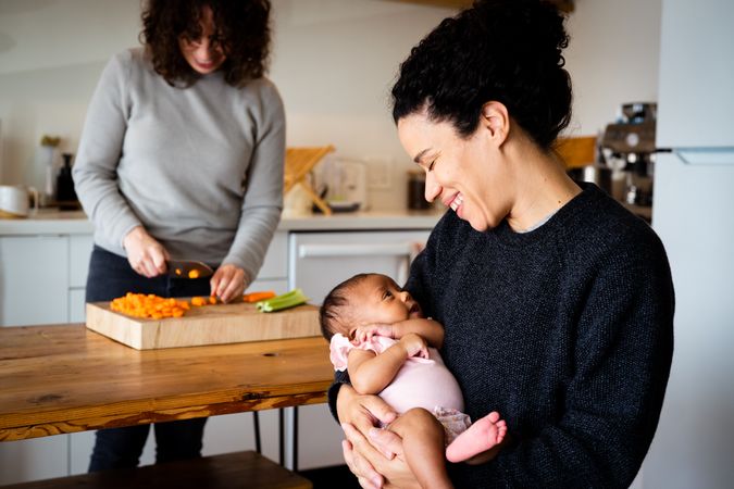 Woman preparing lunch while her partner holds their newborn daughter