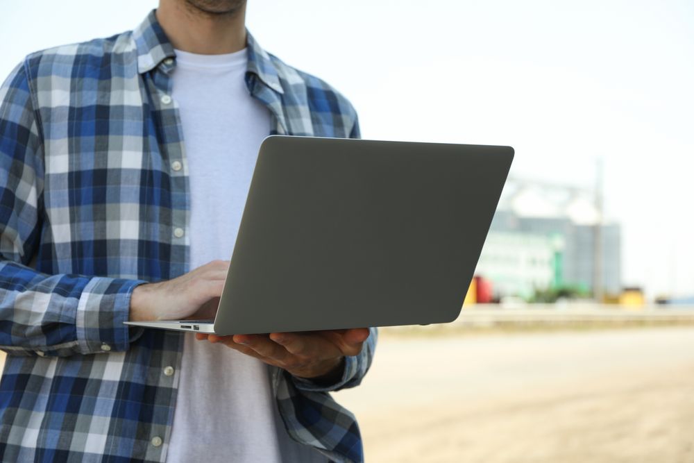 Young man with laptop against grain silos. Agriculture business