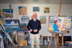 Smiling older male surrounded by paintings in art studio