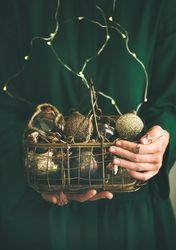 Woman in green dress holding wire basket of gold holiday decorations