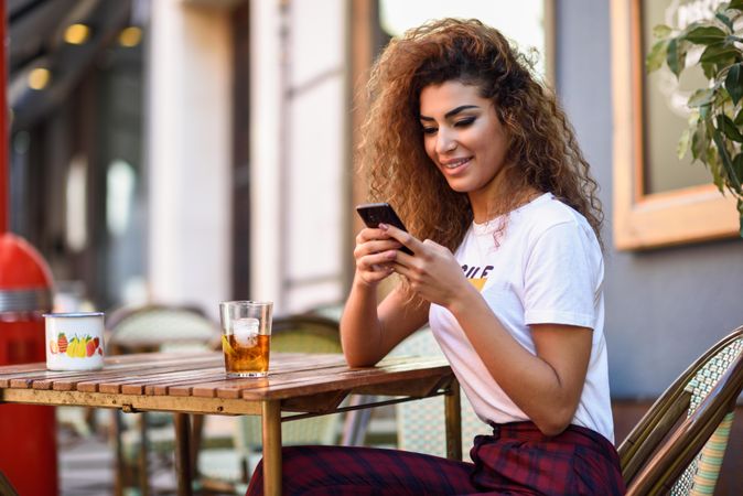 Arab woman in casual clothes texting using her phone on cafe patio