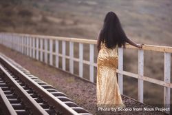 Woman in golden dress standing beside train rail 4M8or5