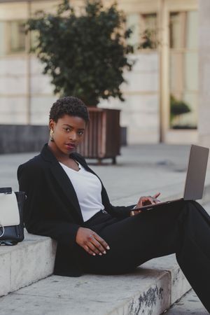 Stylish Black woman with laptop on steps near handbag