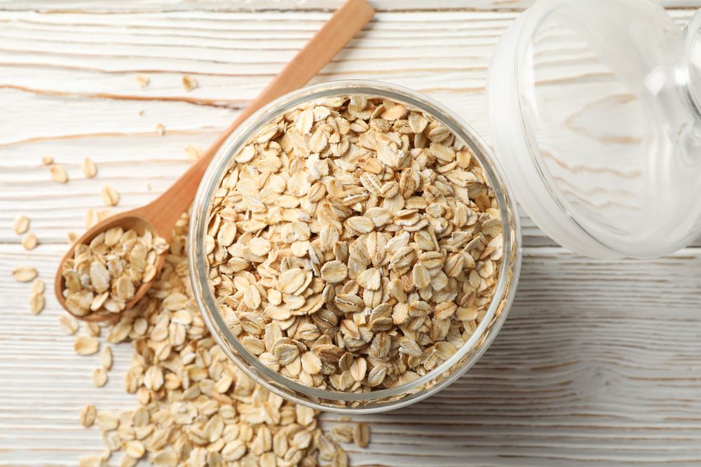 Glass jar with oatmeal and spoon on wooden background, top view
