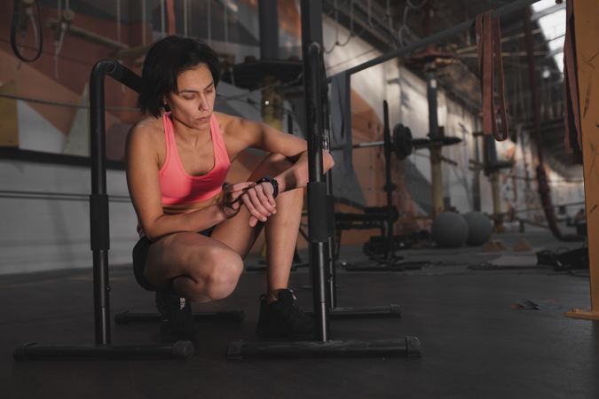 Athletic woman looking at watch between parallel bars in gym