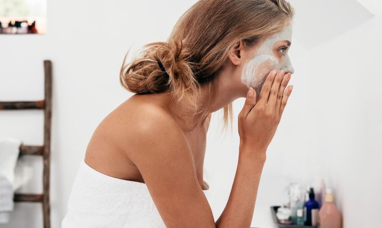 Side view shot of young woman applying facial cosmetic mask in bathroom