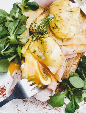 Eggs Benedict with yoke broken with greens, coffee, top view, close up, square crop