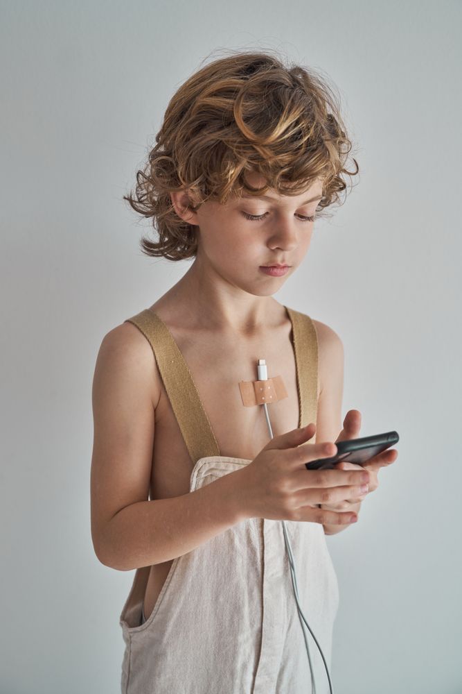 Boy with smartphone and charger glued on chest with plaster