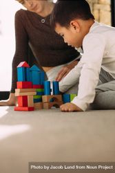Cute child playing with colorful wooden blocks with his mother sitting 5pOyw0
